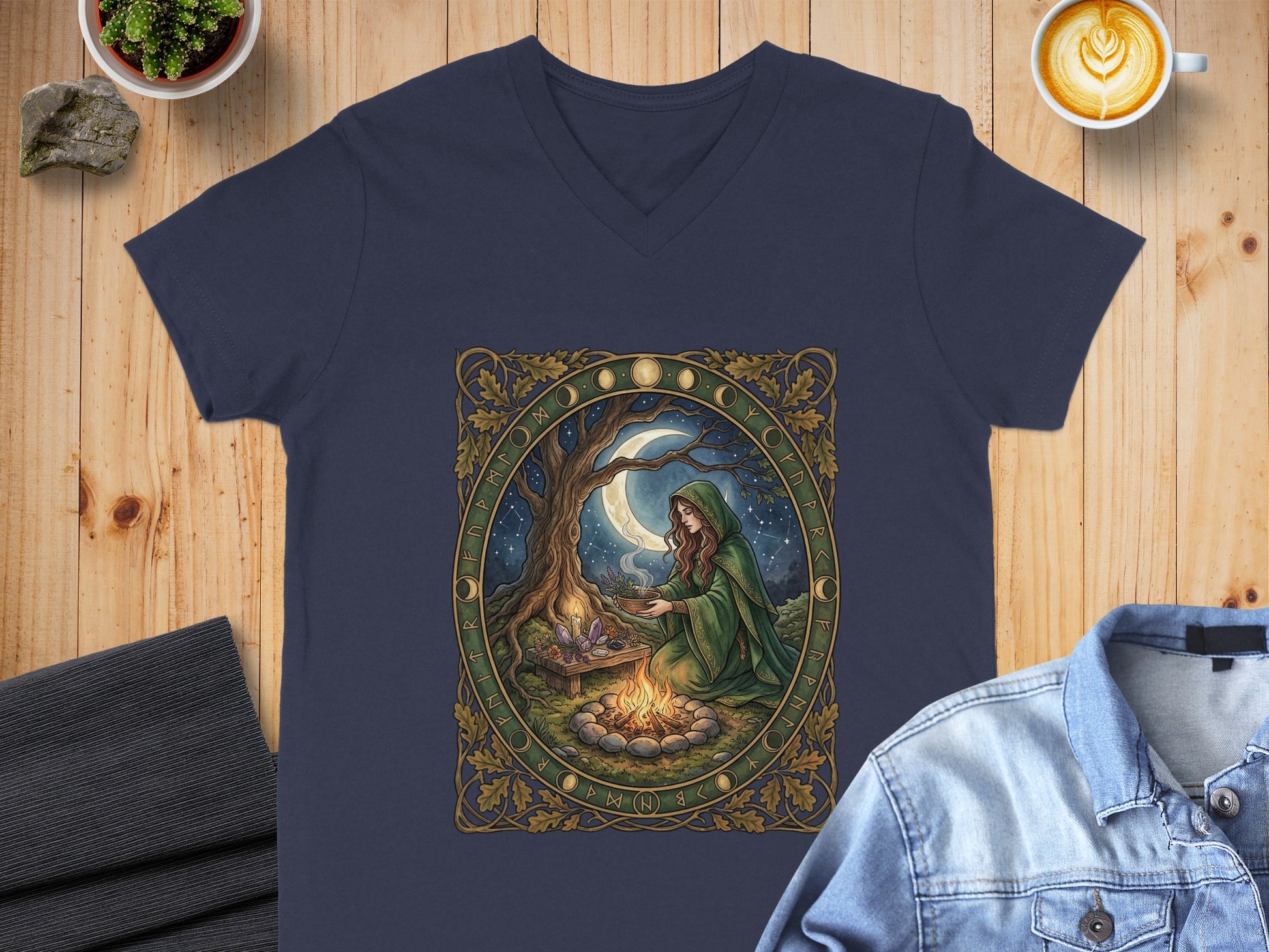 V-neck t-shirt with a woman in a green robe by a campfire, framed by runes and celestial imagery.