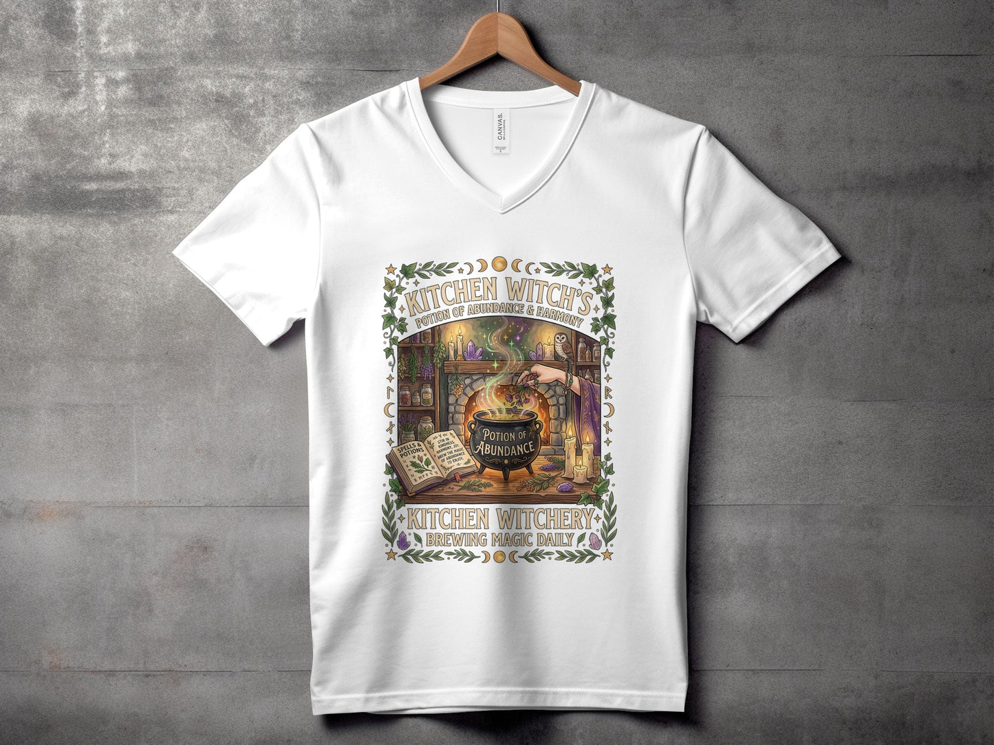White v-neck t-shirt with "Kitchen Witchery Brewing Magic Daily" cauldron graphic.
