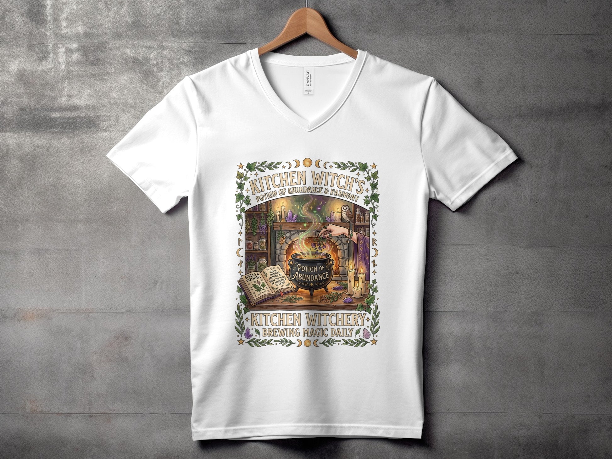 White v-neck t-shirt with "Kitchen Witchery Brewing Magic Daily" cauldron graphic.